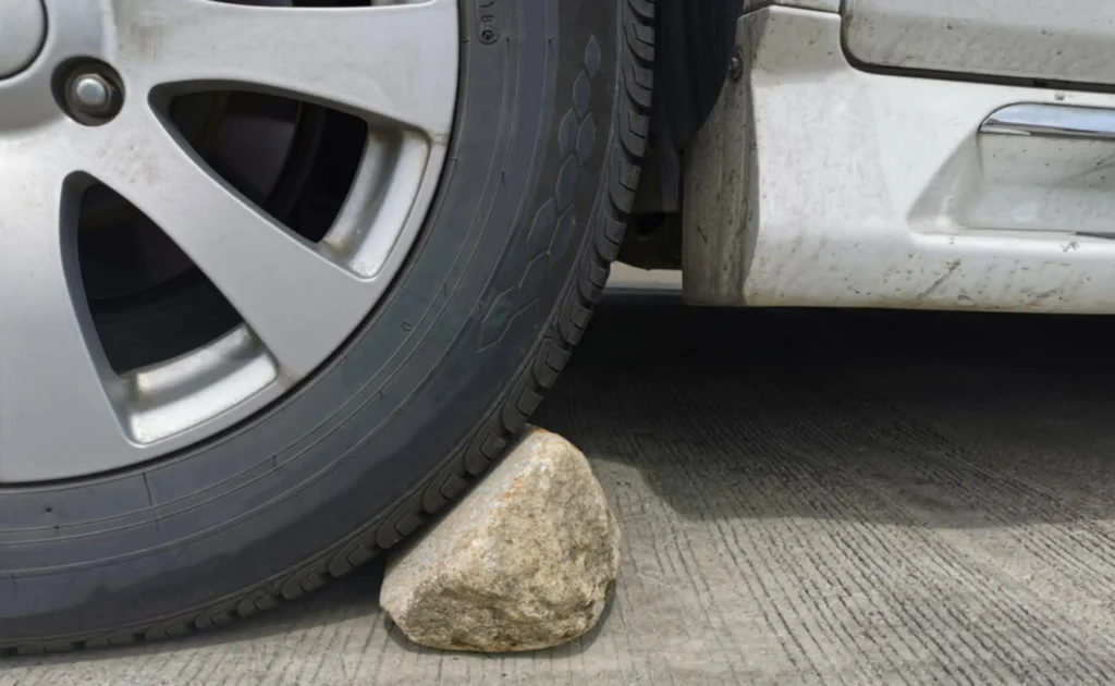 Ganjal roda menggunakan batu atau balok supaya keamanan saat parkir mobil di tanjakan atau turunan aman.